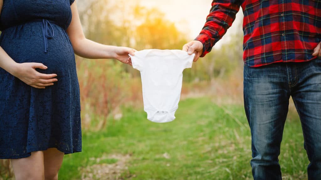 A couple holds a baby's onesie as they stand together.