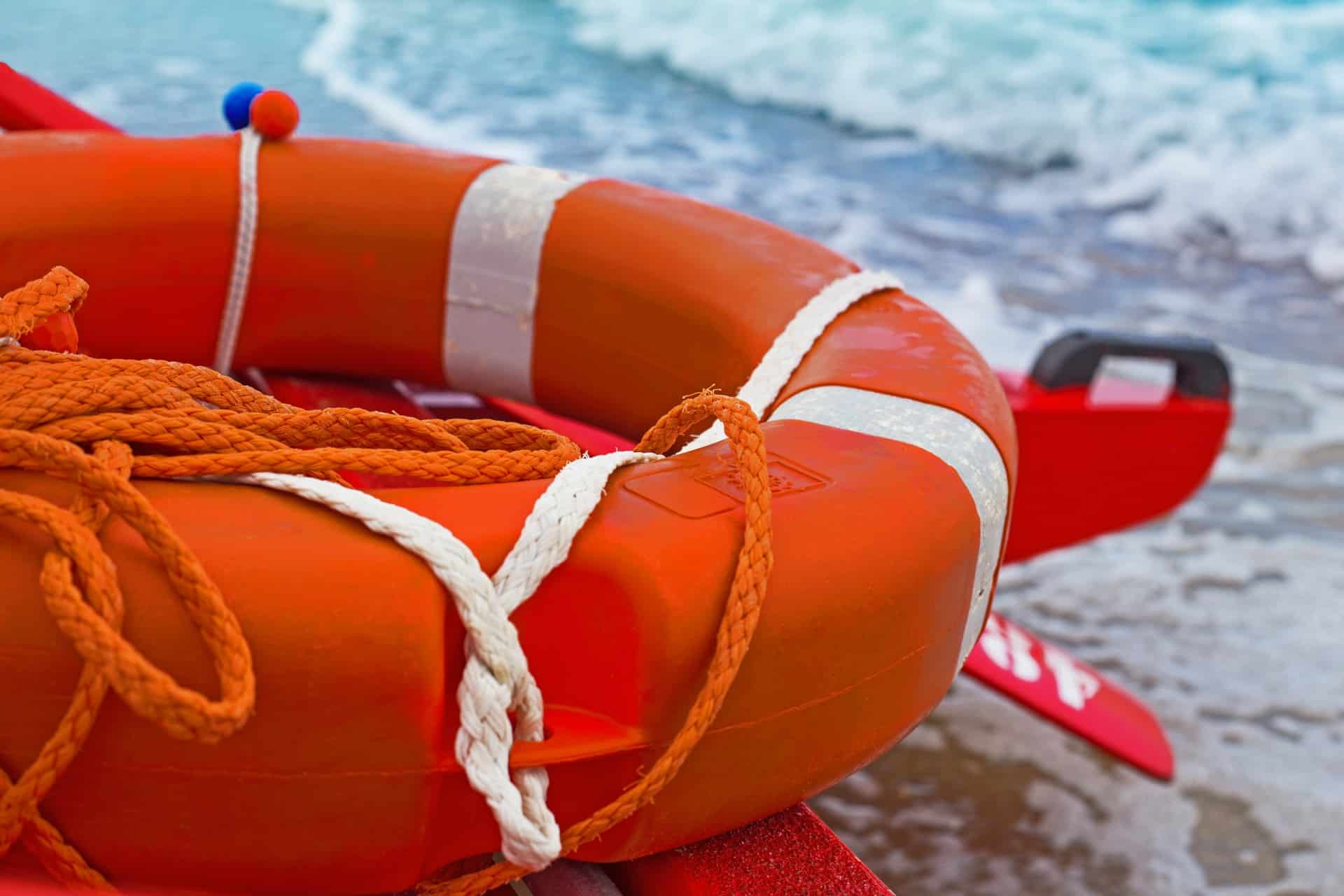 Close up of orange life buoy resting on edge of boat with seashore in background