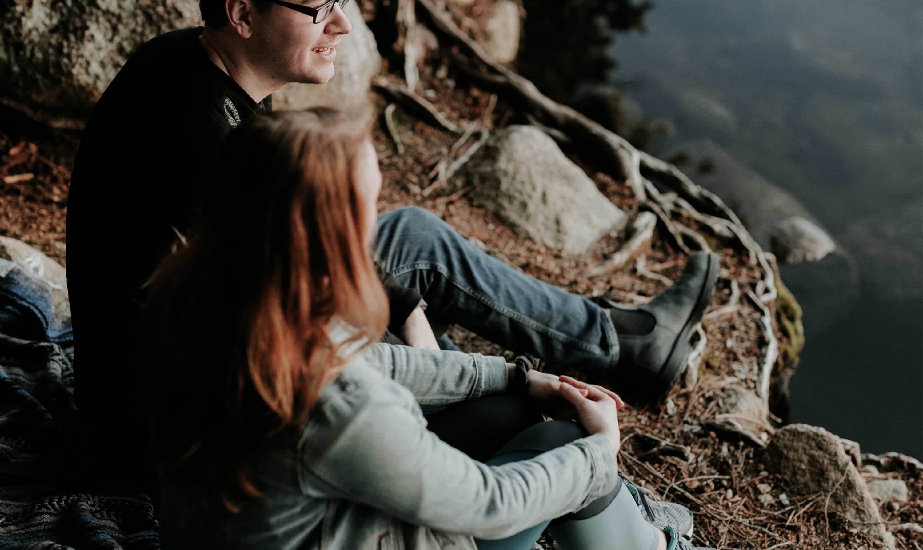 A man and a woman sit outside next to a lake.