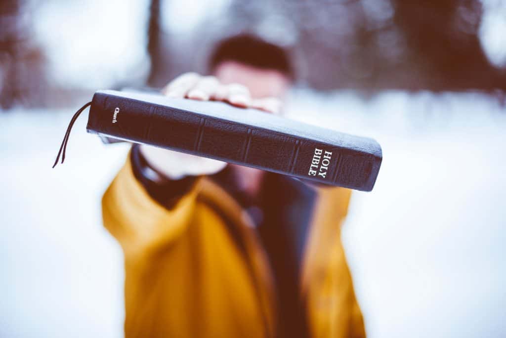 man in yellow jacket confidently holding out his Bible in front of him.