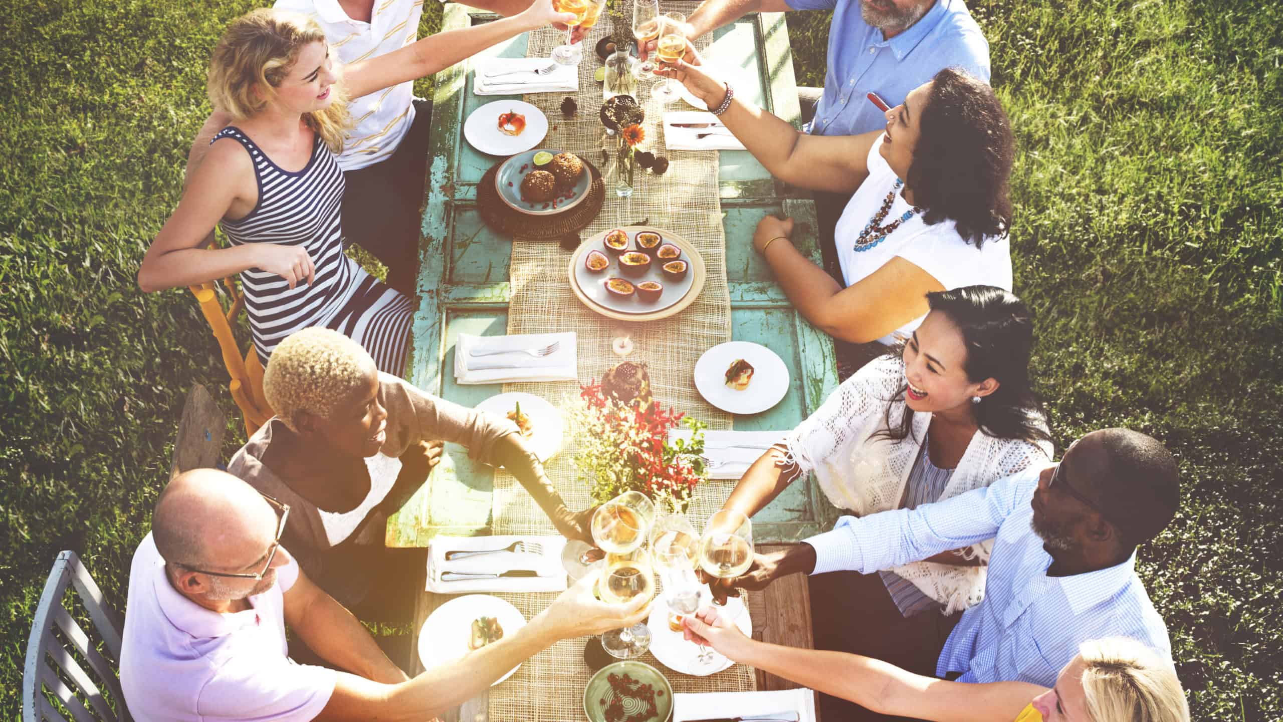 diverse neighbors drinking and eating around table in backyard