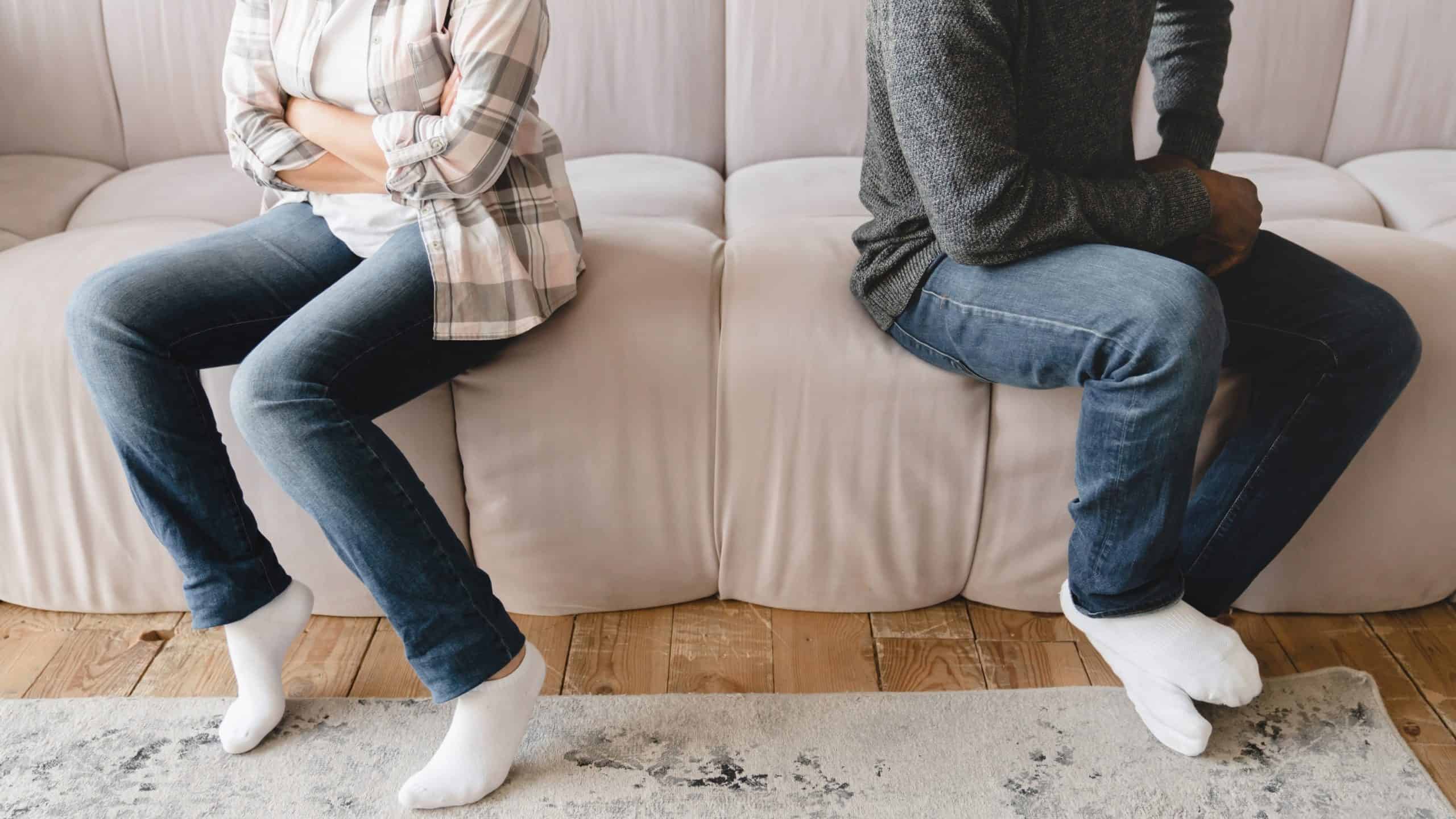 A couple sitting apart on a couch with their arms crossed and looking away from each other, representing a moment of disagreement. This scene can symbolize how healthy conflict in marriage requires space and time for both partners to reflect on their feelings.