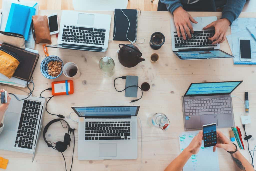 Shown from above, several people sitting at a table working at their laptops