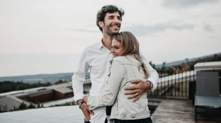 A husband hugs his wife on a cloudy day.