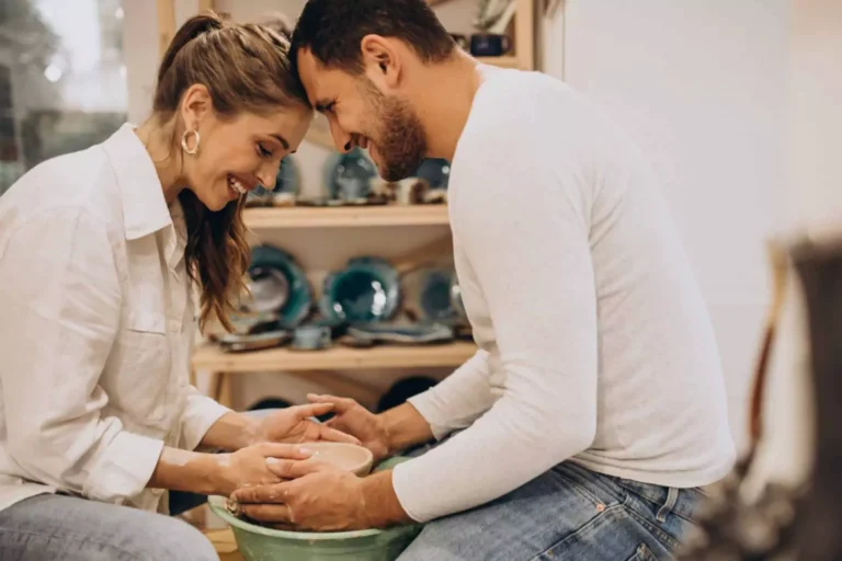 A smiling couple shares a tender moment while working together on a pottery wheel, symbolizing the importance of finding common interests and hobbies with your spouse.