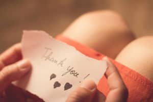 Close up of a woman's hands holding a scrap of paper with a handwritten, affectionate note saying thank you