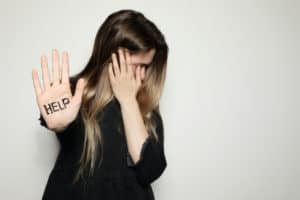 Young woman, a victim of human sex trafficking, holds up her hand for help while hiding her face.