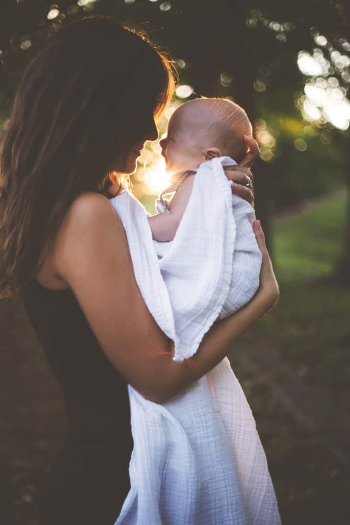 Profile shot of a mother holding her infant close to her face against the backdrop of trees and a sunrise