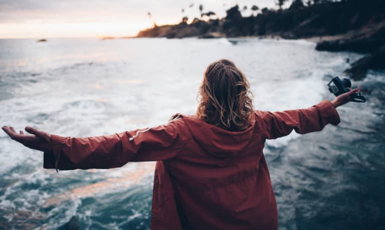 A woman stands at the ocean with her arms open wide.