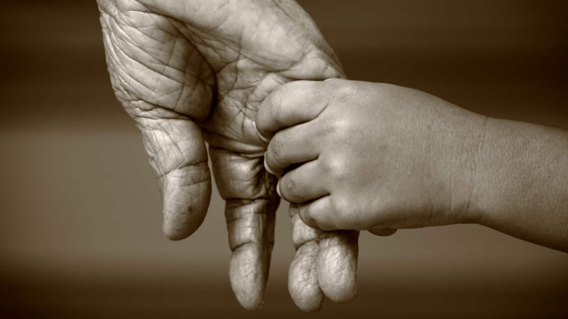 Black and white close-up of a child's hand holding an elderly person's hand