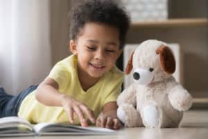 Young girl lying on the floor looking through a book with her teddy bear next to her