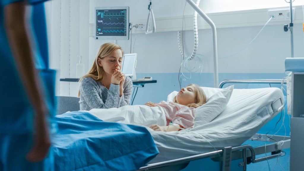 Mom sitting, praying by her young daughter’s bedside in hospital room
