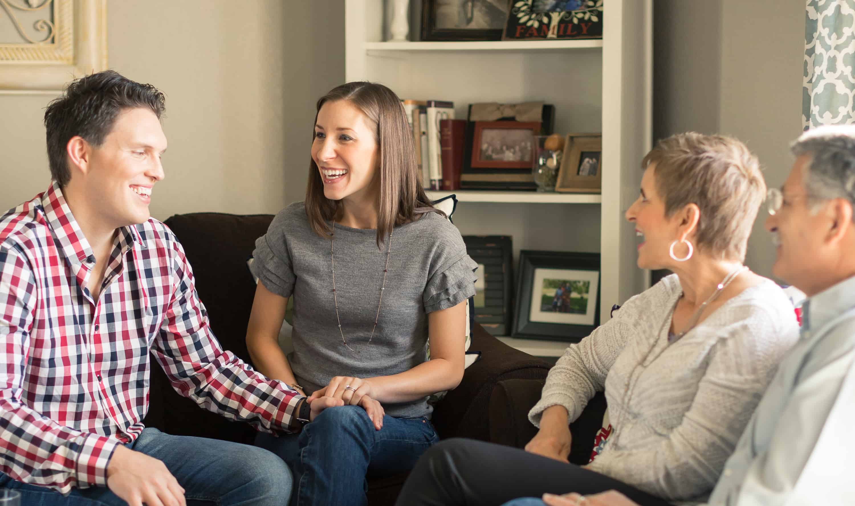 A younger couple sits with an older couple on couches in a living room.