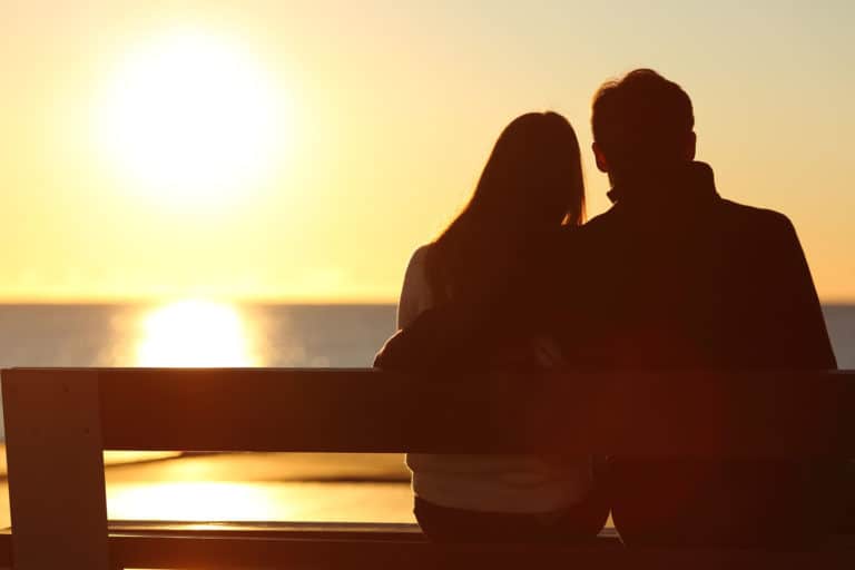 Back view of a couple silhouette hugging and watching sun on the beach