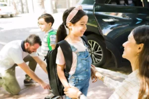 blended family. mom and step dad seeing kids off to school. dad is tying his little boy's shoe while mom is talking to her little gir.