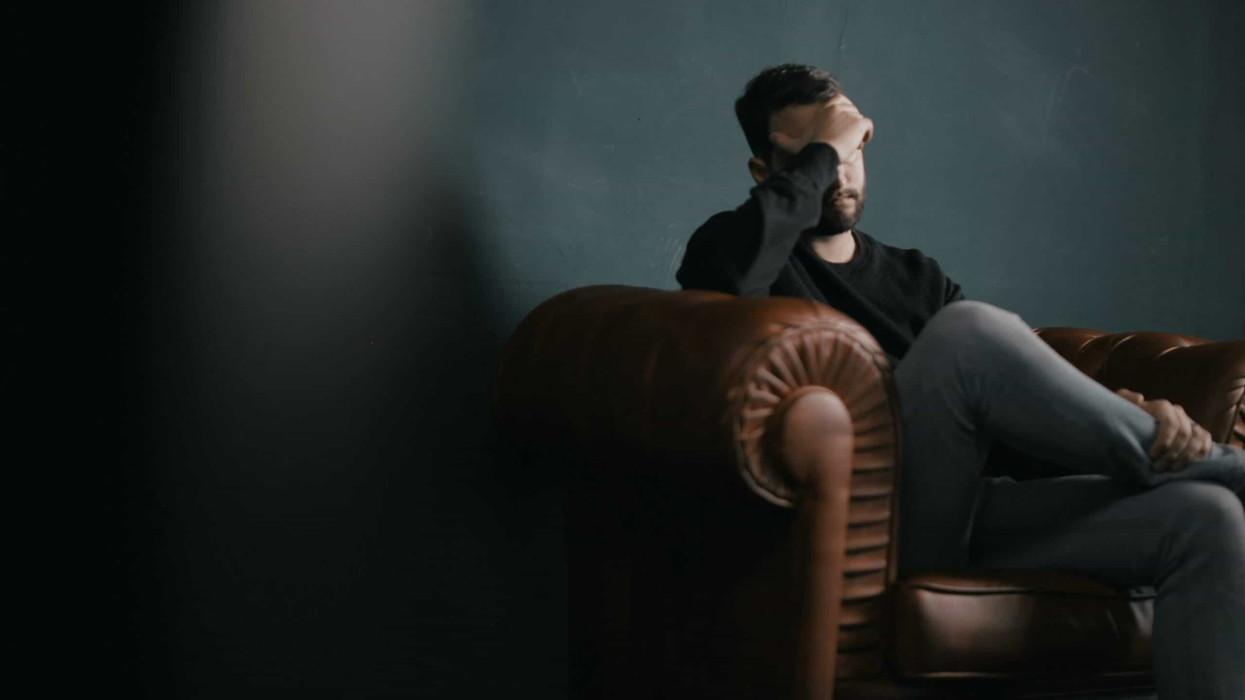 man on leather sofa head in hands