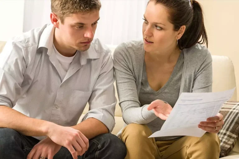 A couple sits on a couch looking concerned while reviewing a financial document, illustrating the impact of destructive attitudes that can keep you in debt.