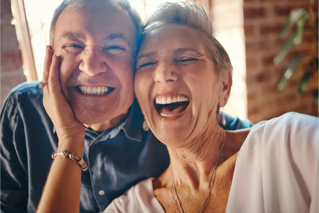 A husband and wife facing the camera, laughing together, embodying the phrase “laughter is the best medicine.”