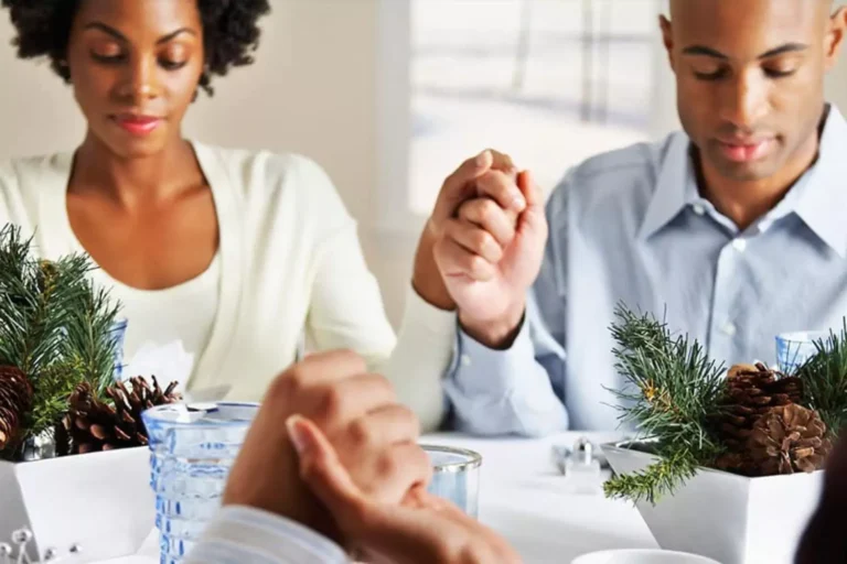 Family saying grace around the dinner table, with focus on one couple holding hands, showing the importance of giving thanks together for what God gives us.