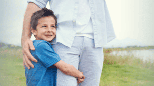 parenting, protecting kids: happy little boy in a blue tshirt hugging his daddy's let