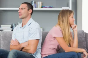 Fighting fair is key to resolving conflicts in marriage. A young couple sits on the couch with their backs to each other.