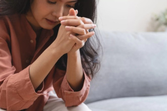 Woman sitting with folded hands in prayer, illustrating how to say prayers for your children with heartfelt intention.
