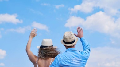 Middle-aged couple with backs to us wave goodbye to children as they enter empty-nest years. The sky is blue and beautiful, symbolizing hope for a full marriage and a happy future.