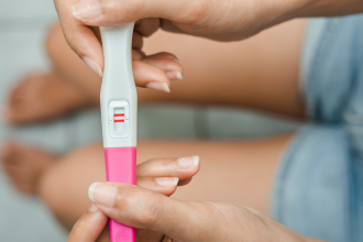 A young woman sits holding a positive pregnancy test, wondering how to go about dealing with unplanned pregnancy.