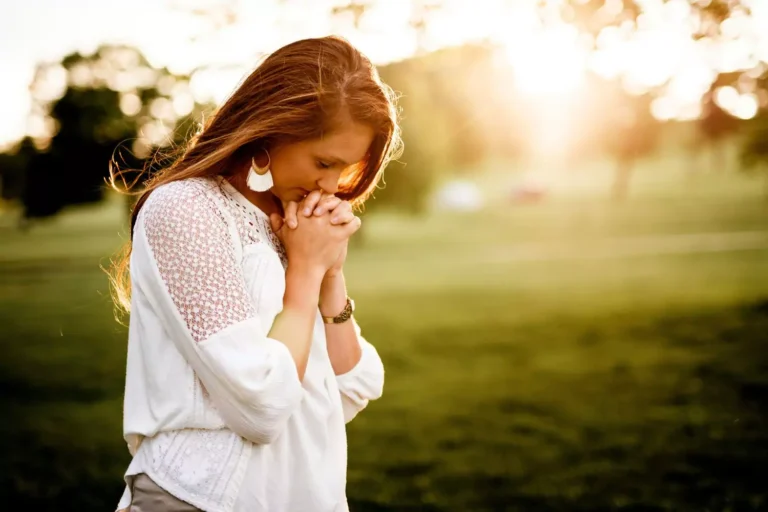 A woman standing outside at sunset with her hands clasped in prayer, symbolizing reflection on her spiritual temperament.