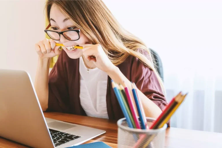 A woman biting a pencil while eagerly looking at her laptop screen, taking a spiritual temperament quiz.