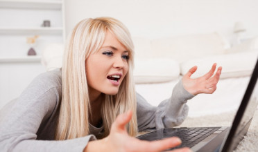 Young, blonde woman lying in front of her computer, expressing frustration at what she's seeing