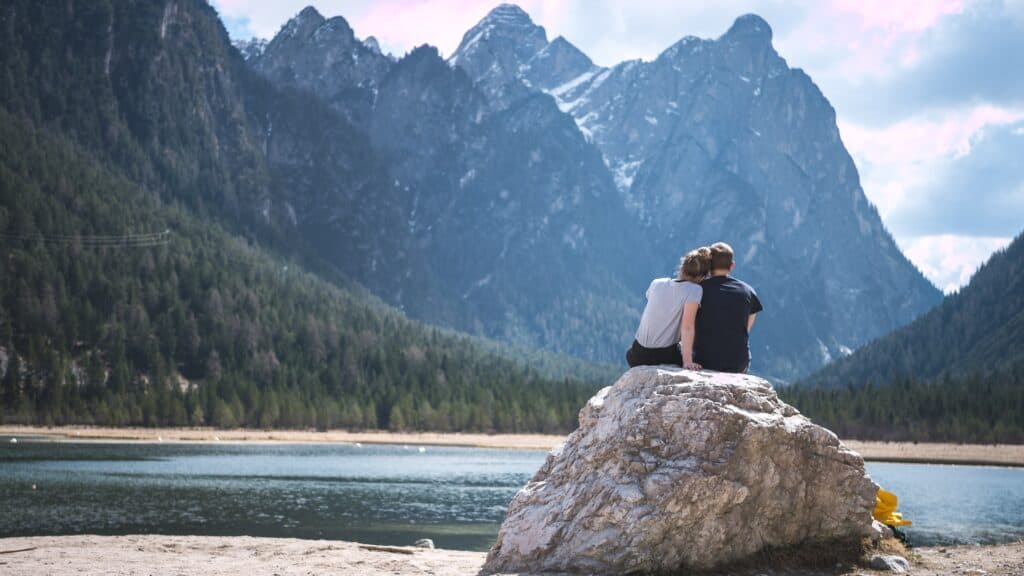 A couple sits on a rock looking at a high mountain range