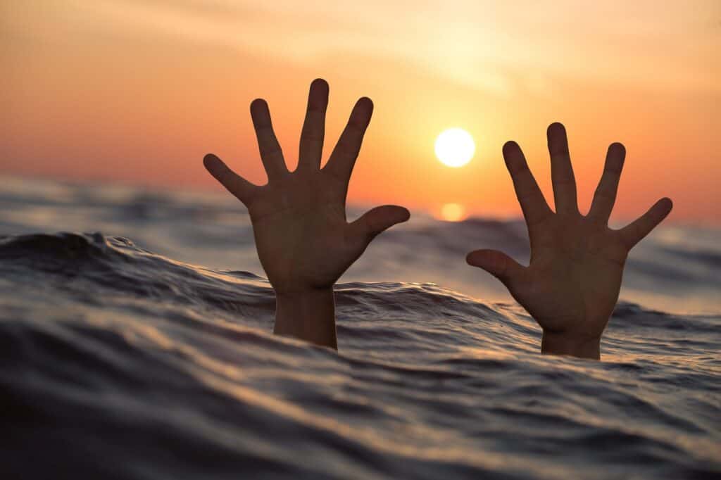Person drowning is holding hands above water