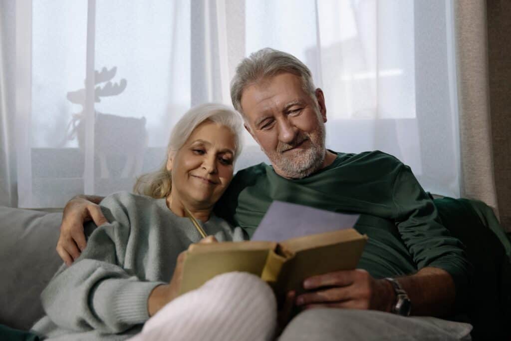 Grandparents sitting on the couch together looking lovingly at a letter in a book