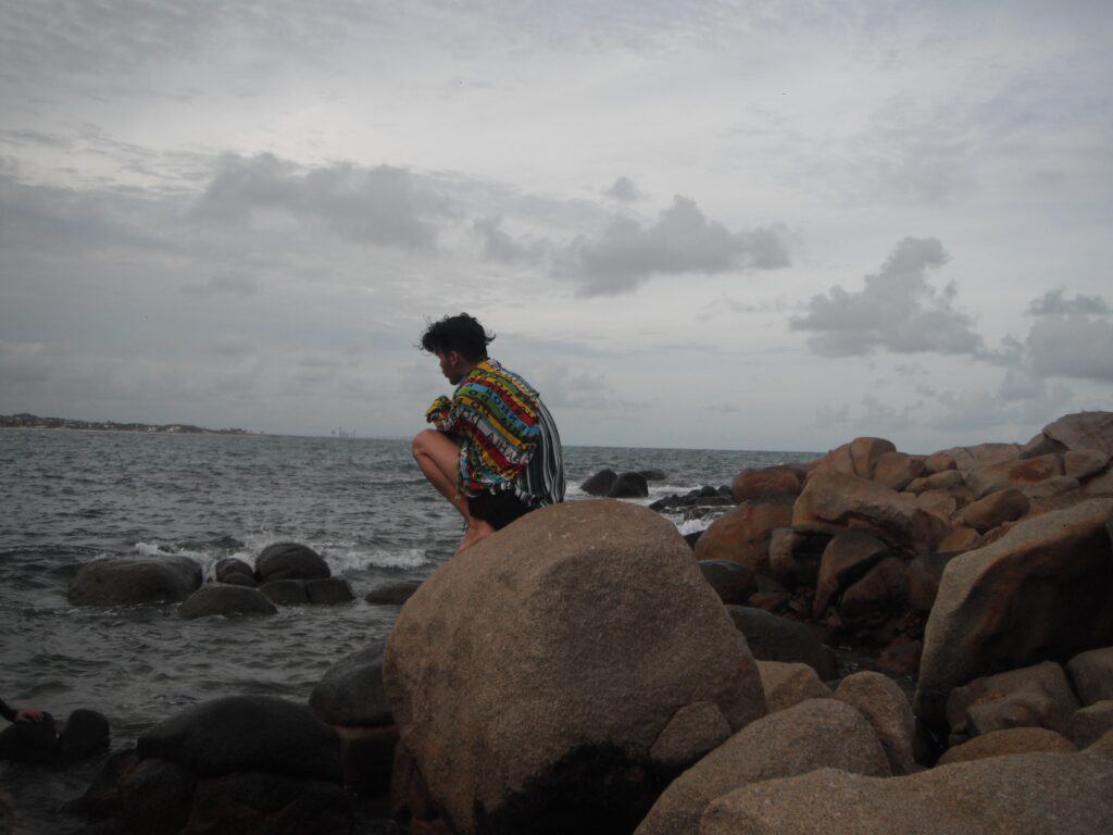 anxious-looking man sitting on a rock overlooking the ocean