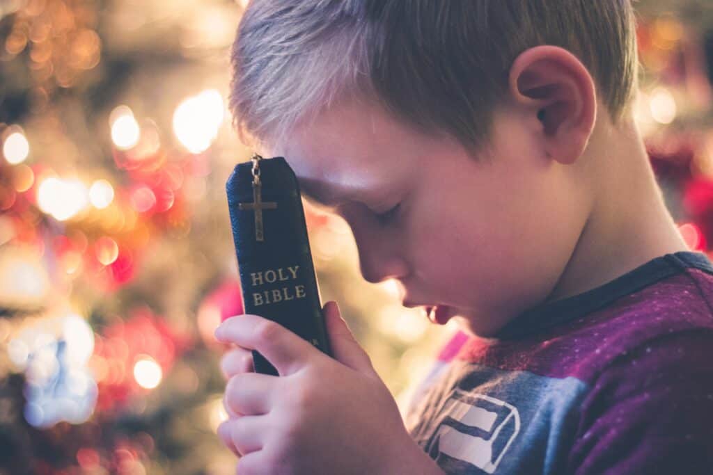 child holding Bible in front of Christmas lights