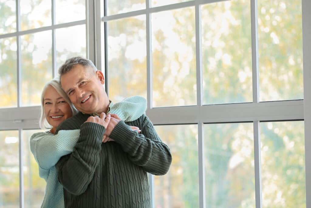 happy older couple in house by big window