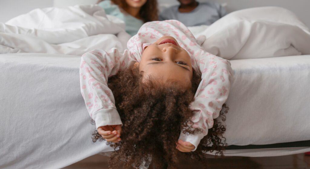 Little girl in parents' bed, mom and dad in background