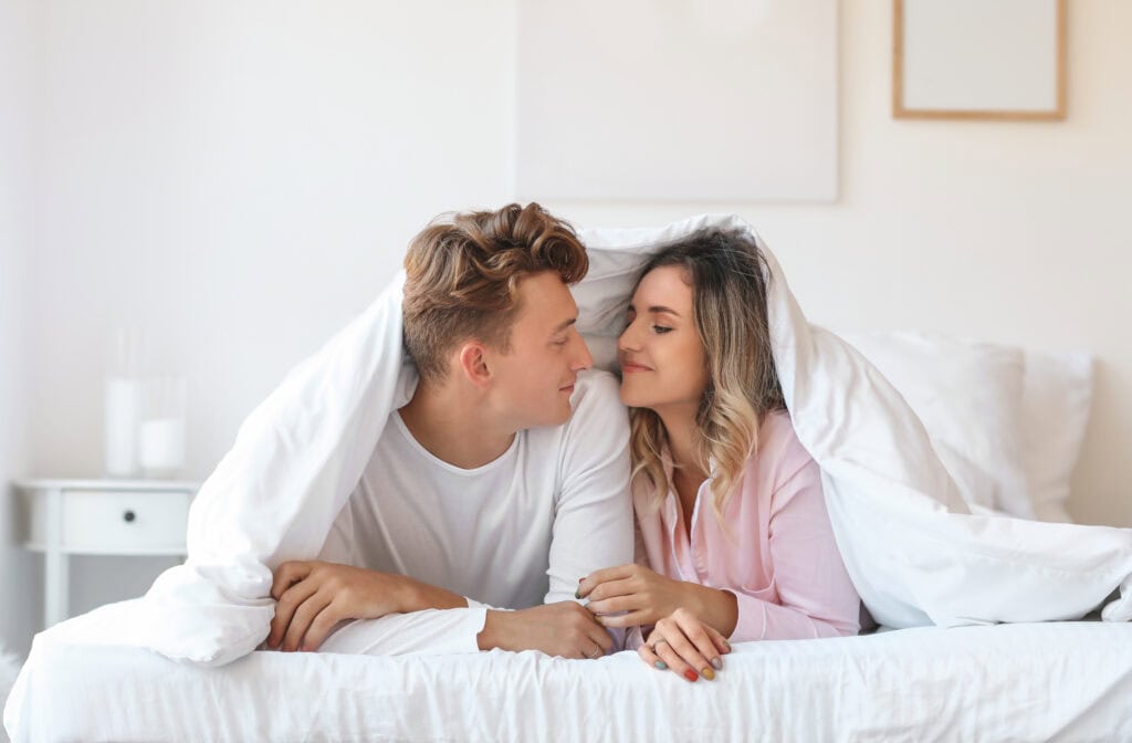 couple dressed lying together under sheet on bed