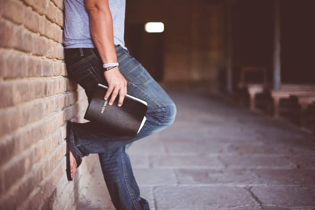 young man leaning on brick wall holding Bible at his side