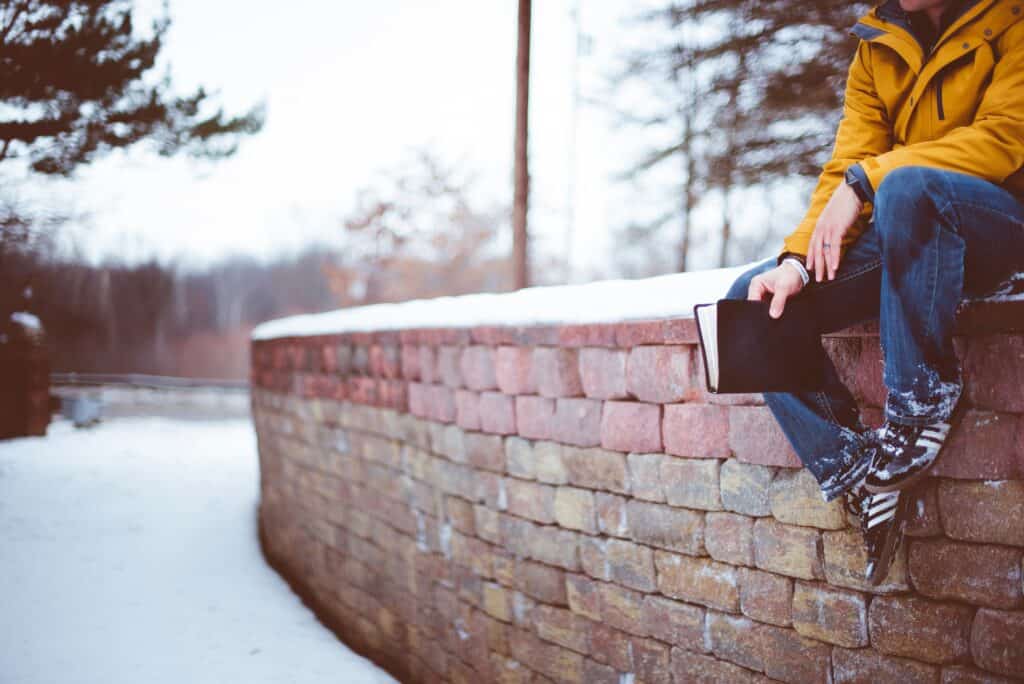 young man sitting on brick wall holding Bible