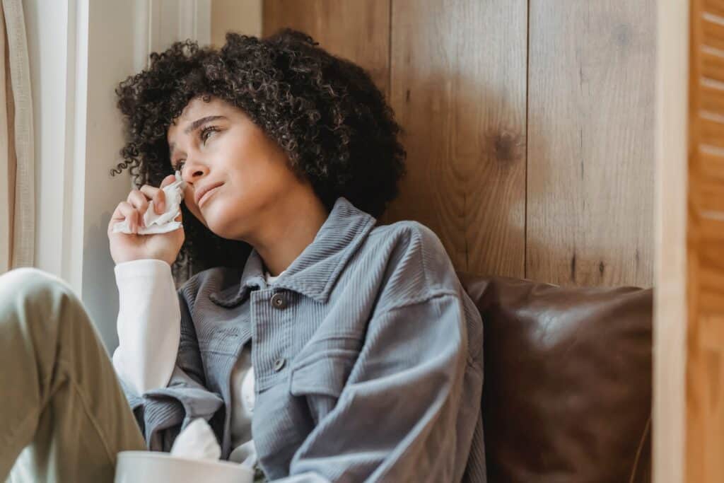 Woman sitting in a corner wiping tears from her eyes