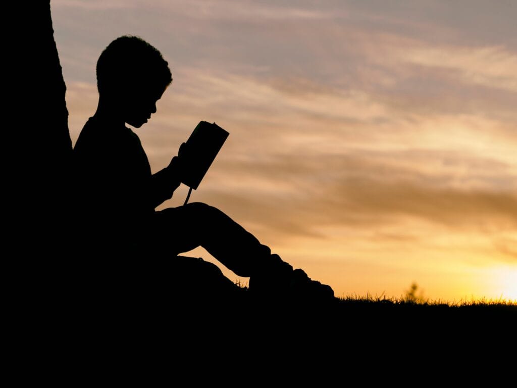 Boy reading Bible with sunset in background