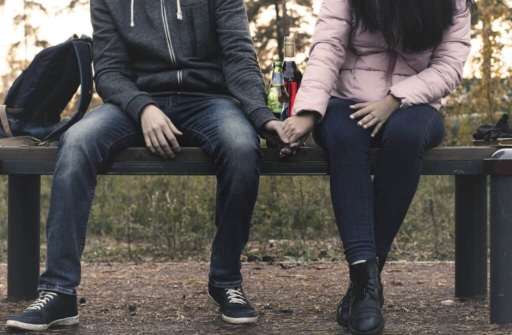 legs arms of couple holding hands, alcohol bottles in background