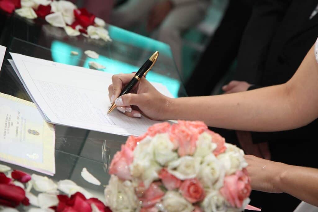 bride's hand signing marriage license flowers in foreground