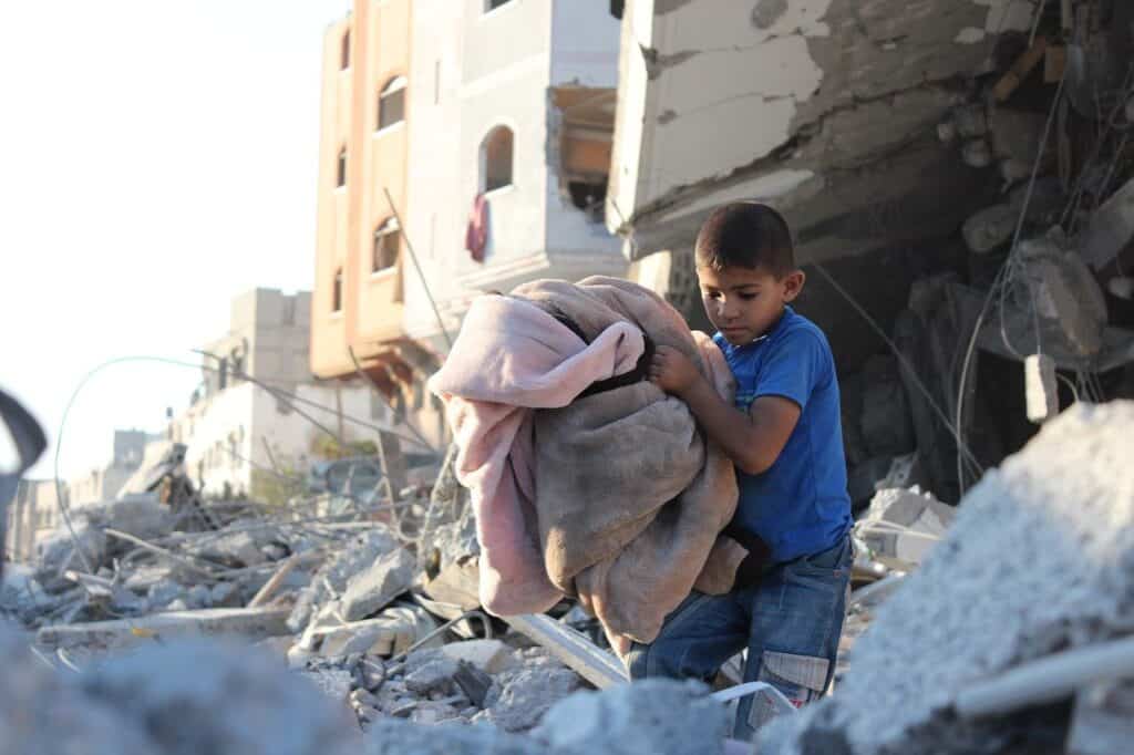 child in destroyed area carrying blanket
