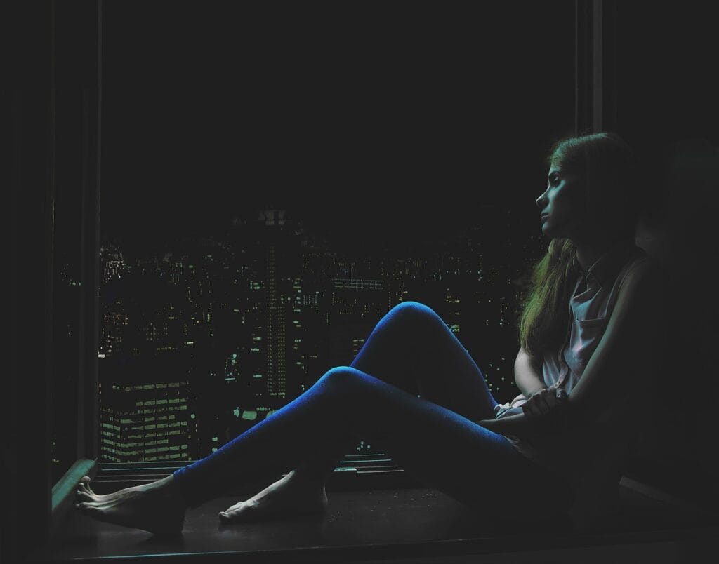 sad girl sitting in darkness looking out at city skyline