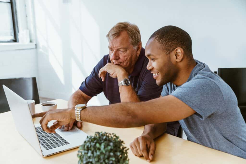 younger man helps older man with computer