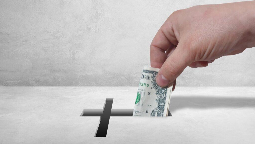 hand putting money in box with cross shaped opening