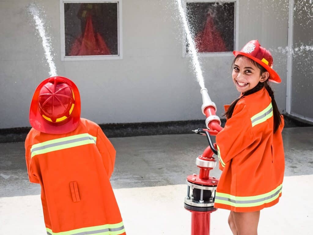 Little girl dressed as firefighter with hose